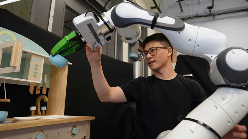 Graduate student Felix Yanwei Wang nudges a robotic arm that is manipulating a bowl in a toy kitchen set up in the group’s lab. Using the framework Wang and his collaborators developed, slightly nudging a robot is one way to correct its behavior. Credit: Melanie Gonick, MIT