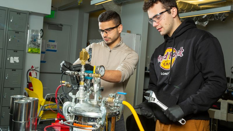 MIT engineers Aly Kombargi (left) and Niko Tsakiris (right) work on a new hydrogen reactor, designed to produce hydrogen gas by mixing aluminum pellets with seawater. Photo: Tony Pulsone