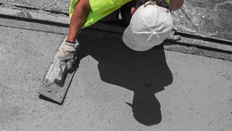 A construction worker levels a concrete pavement. (stock.adobe.com)