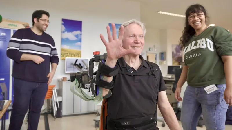 Wolfgang Korisanski is one of the 24 patients who have already tested the new exoskeleton and electrical stimulation system for a study. In the background: Hossein Kavianirad (left) and Neha Das, researchers from Prof Sandra Hirche's department